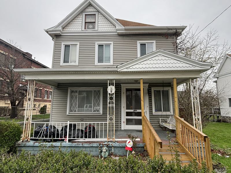 Before renovation: front of the house with an old porch and overgrown yard, house on 1128 McCleary St, McKeesport PA