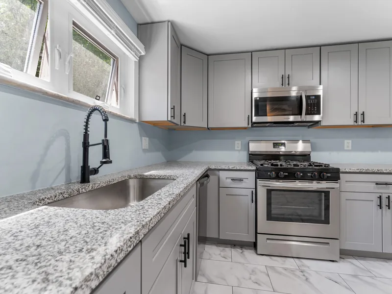 After renovation: kitchen with gray cabinets, granite counters and stainless steel appliances
