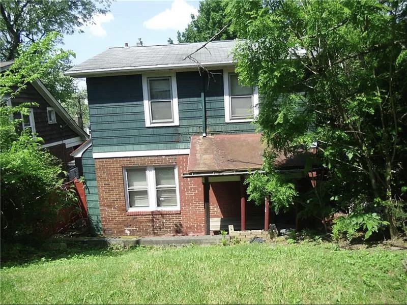 Before renovation: back of the house with dark green siding and an overgrown yard, house on 2301 Fairland St, Pittsburgh PA