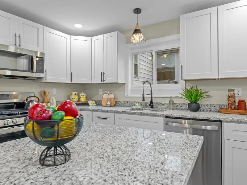 After renovation: white kitchen with a granite island and stainless steel appliances