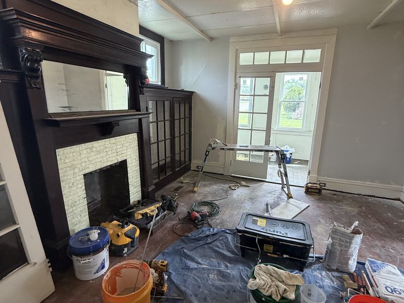 Before renovation: living room with the original fireplace mantel at the start of the renovation, tools and buckets on a bare floor, house on 801 Vine St, Liberty PA