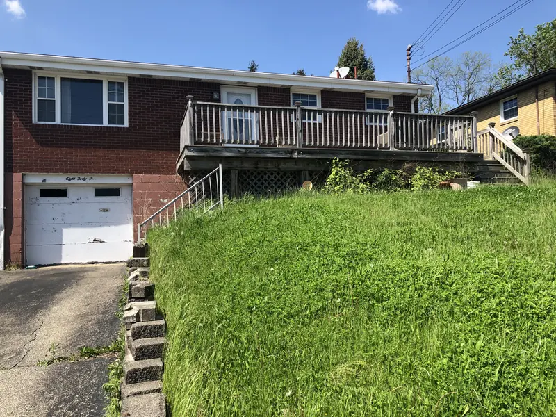Front of a West Mifflin house on Joyce Dr before renovation, with an overgrown slope, worn deck and old garage door